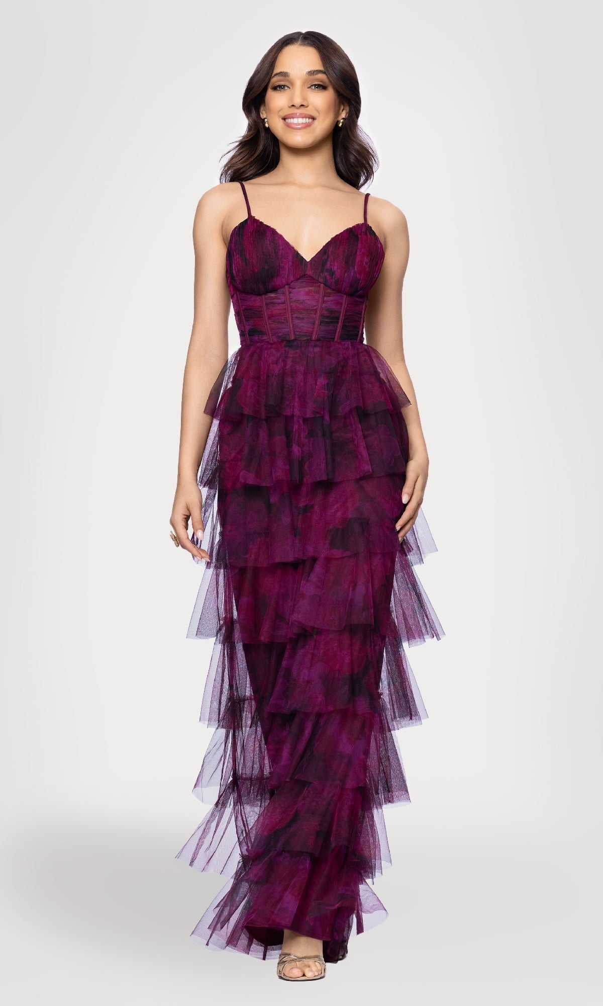 A woman wearing the Blondie Nites 5778BN Wine Red Ruffle Formal Gown in Wine/Multi, featuring a sleeveless, tiered design with spaghetti straps and a fitted bodice, stands against a plain light background.